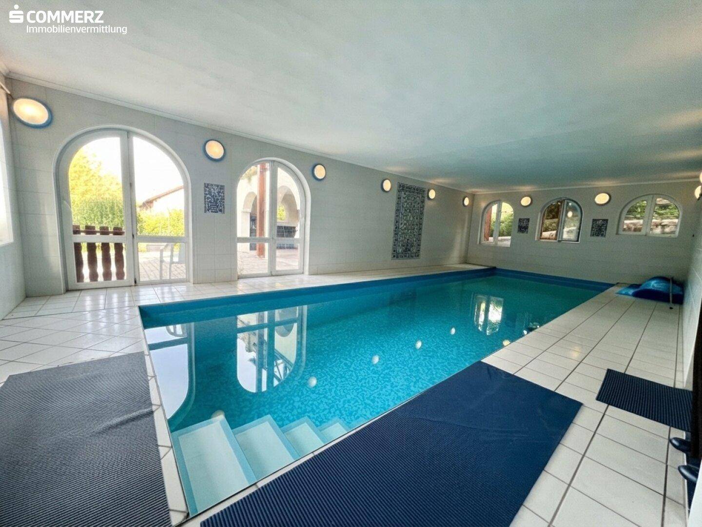 Großes Hallenbad mit weiß gefliestem Boden und Zugang zu einem Außenbereich, ideal für Sport und Entspannung.