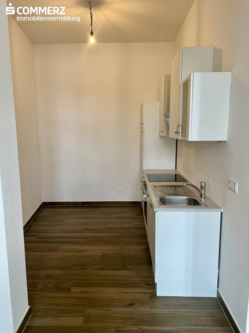Helle, leere Küche mit einfacher weißer Küchenzeile, Spüle und dunklem Holzfußboden.
