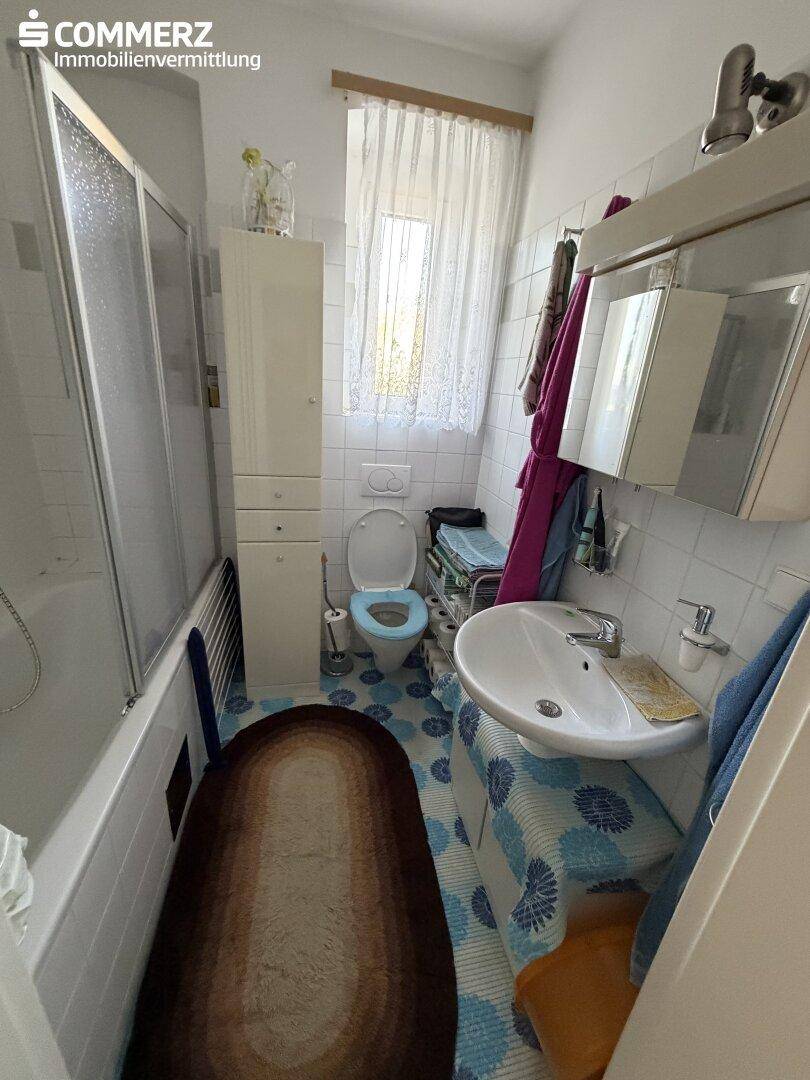 Kleines Badezimmer mit Badewanne, Dusche, WC und Fenster in hellem Design.