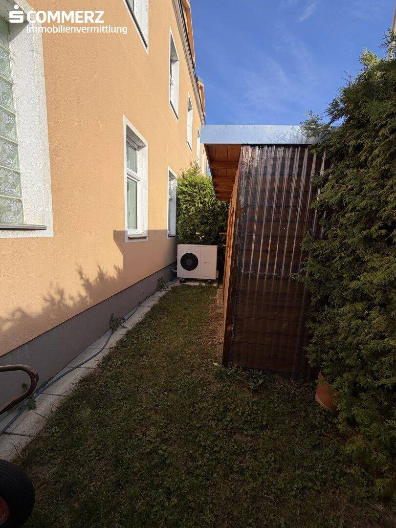 Seitenansicht des Hauses mit Wärmepumpe und kleinem Schuppen im Gartenbereich.
