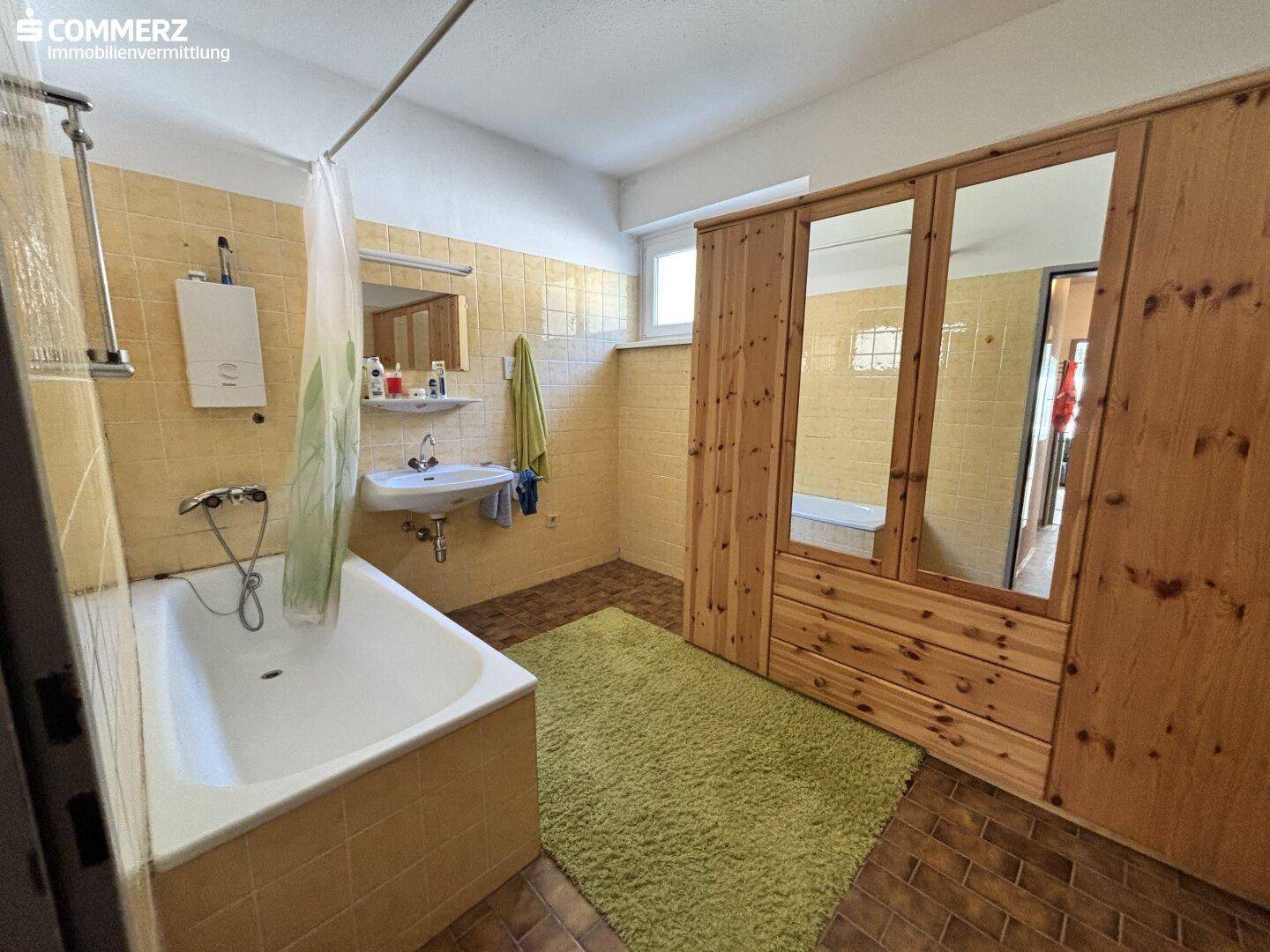 Badezimmer mit gelben Fliesen, Badewanne und einem Holzschrank mit Spiegeltüren.