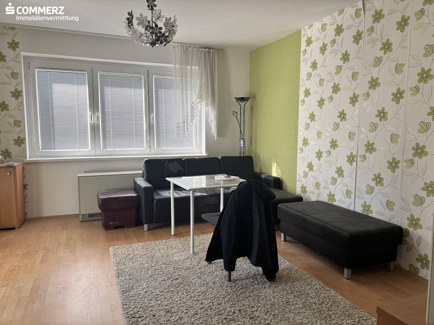 Geräumiges Wohnzimmer mit heller floraler Tapete, Parkettboden und einem bequemen Sofa.
