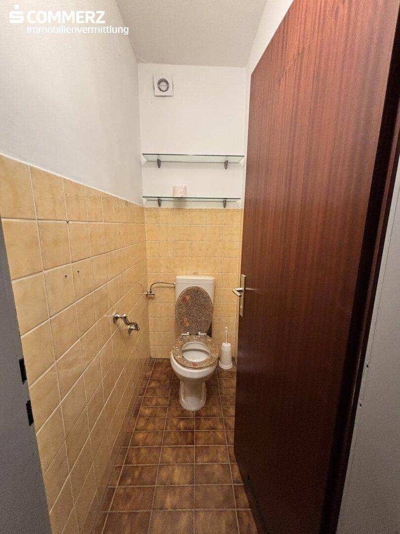 Separates WC mit beigefarbenen Wandfliesen, Toilette und einem kleinen Fenster.