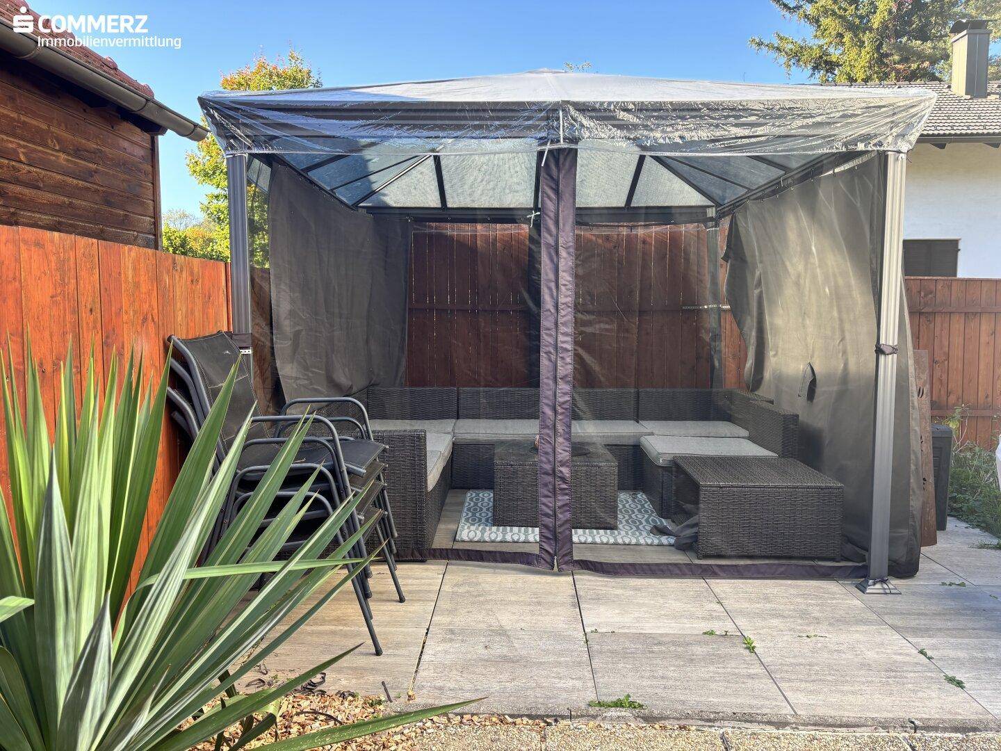 Gemütlicher überdachter Sitzbereich im Garten mit Rattanmöbeln und Sichtschutz.