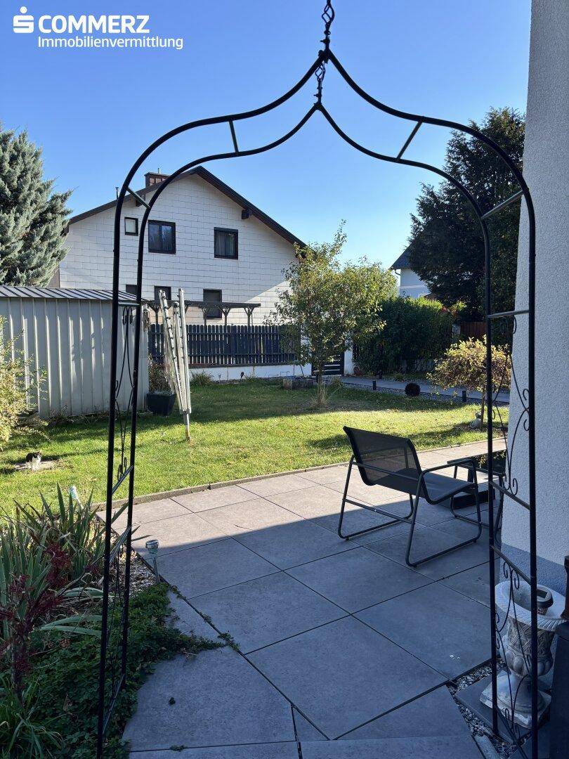 Gepflasterte Terrasse mit Gartenmöbeln und einem dekorativen Metallbogen im Außenbereich.