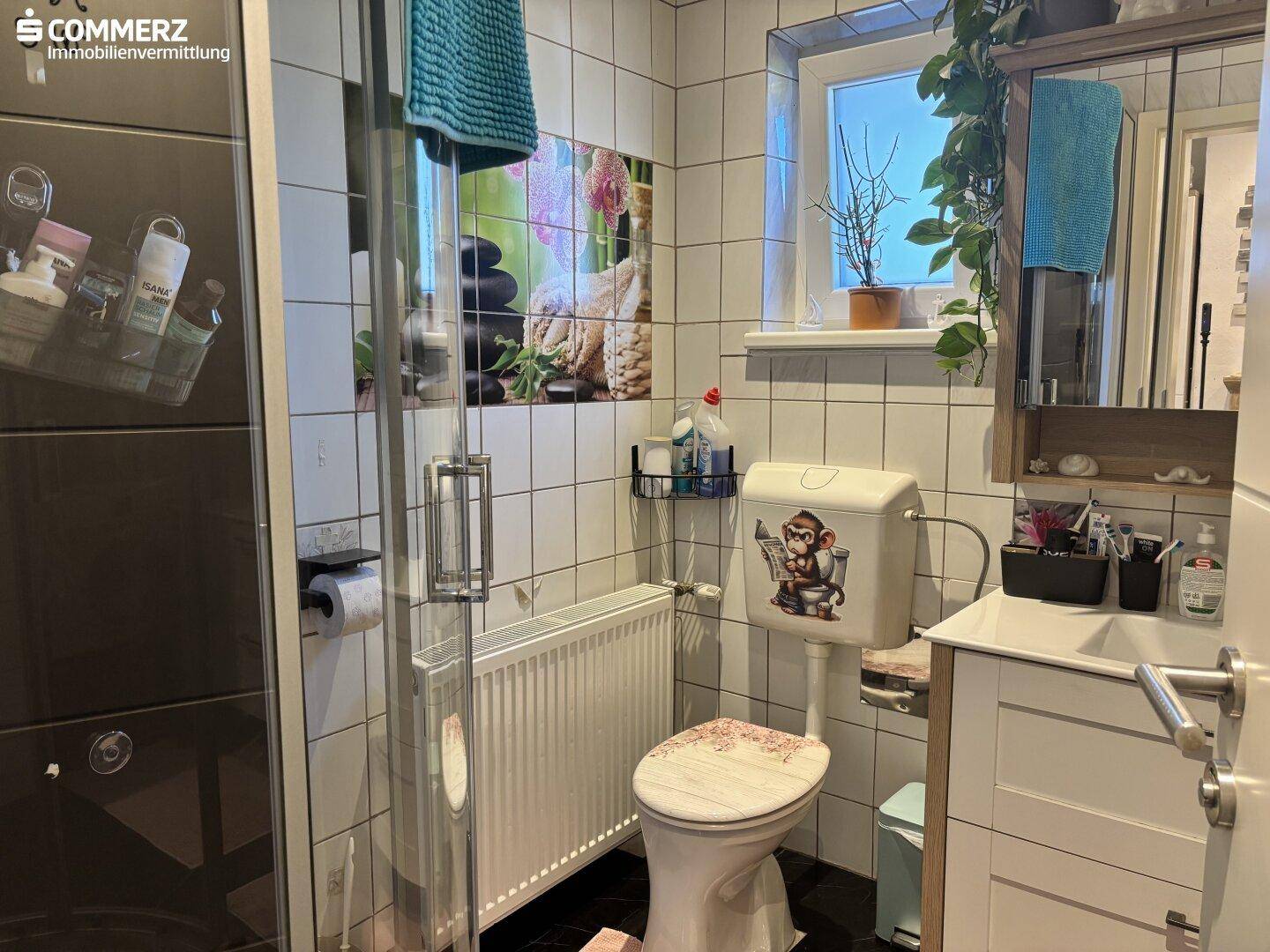 Helles Badezimmer mit Duschkabine, WC, Waschbecken und Fenster.