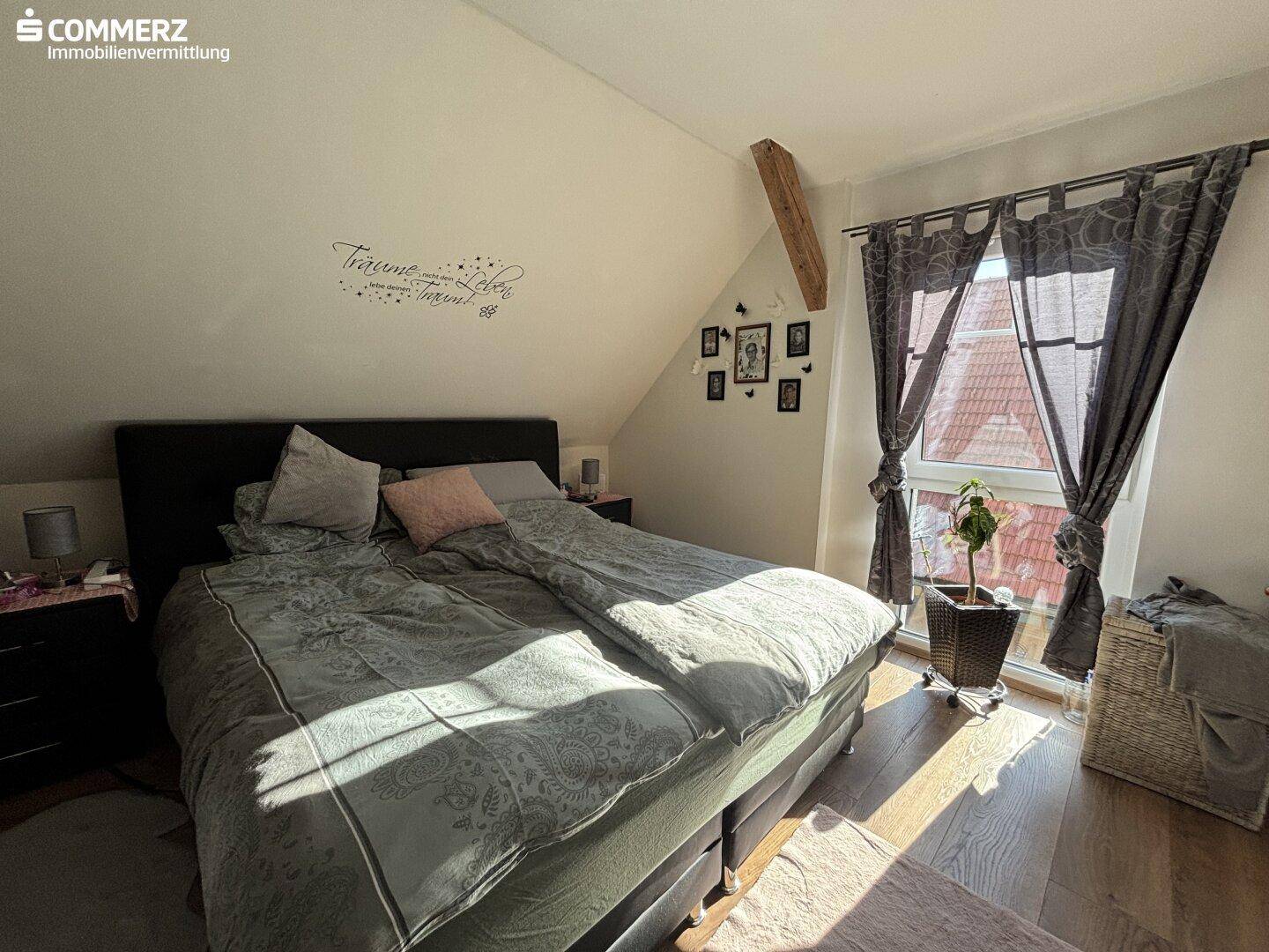 Gemütliches Schlafzimmer im Dachgeschoss mit Doppelbett, Holzbalken und Fenster.