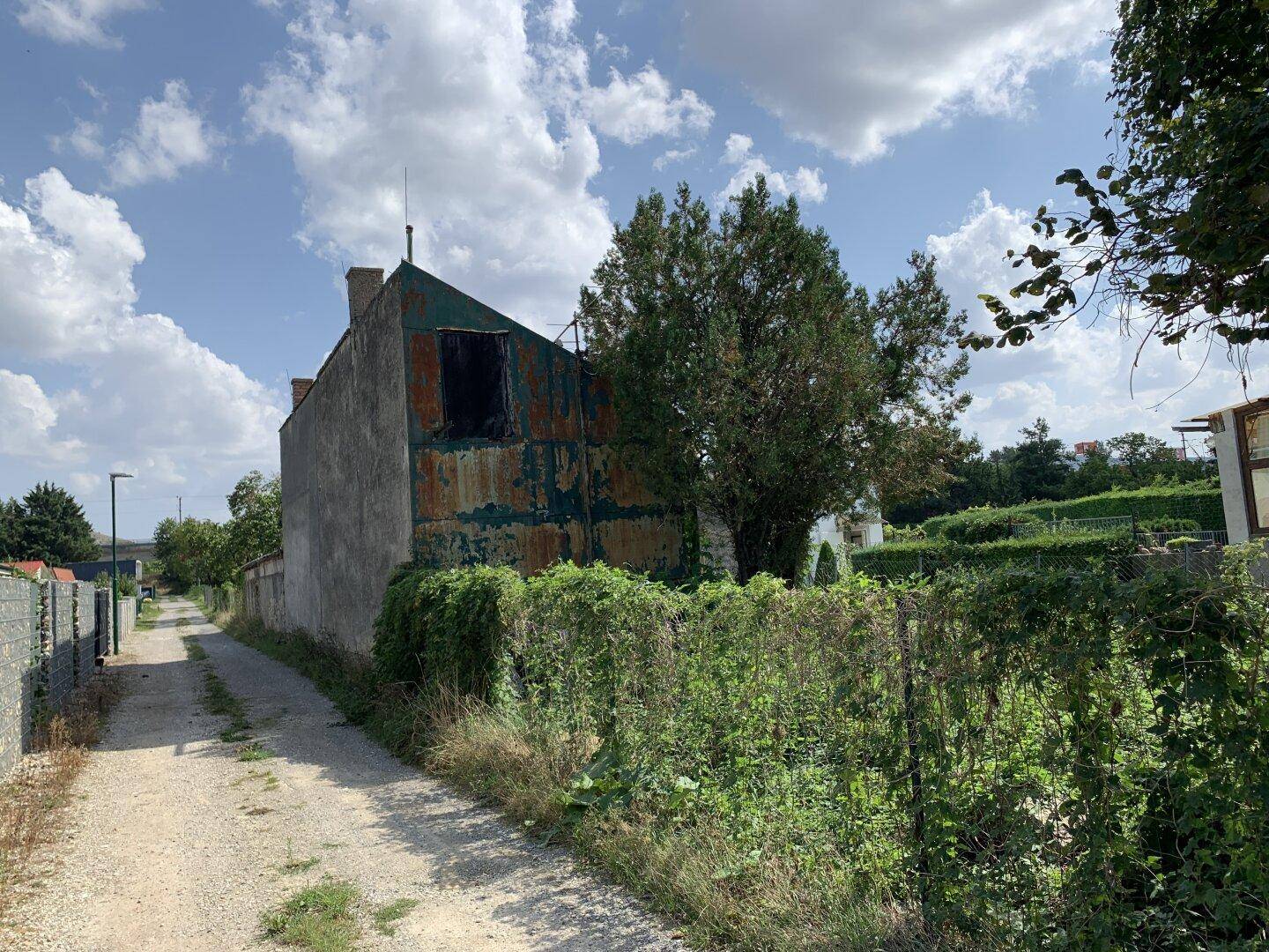 Rückansicht eines älteren Gebäudes mit verrosteter Fassade und einem unbefestigten Weg daneben.