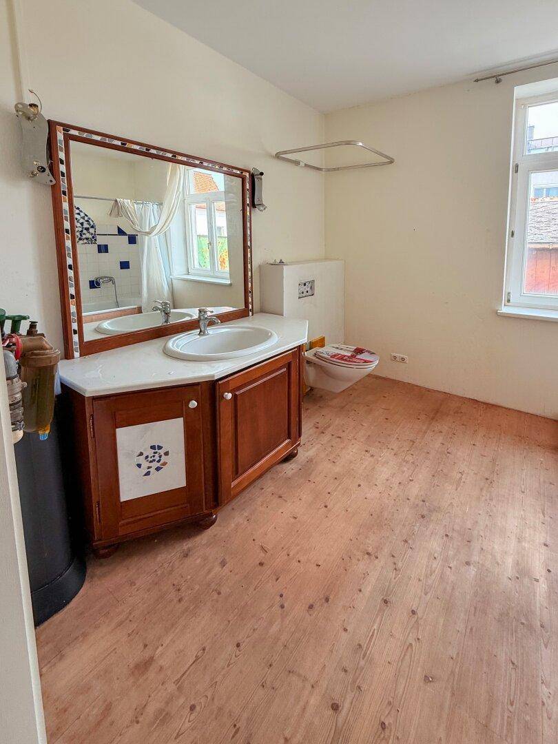Badezimmer mit Holzwaschtisch, Spiegel und Toilette, sowie einem Fenster für natürliche Belüftung.