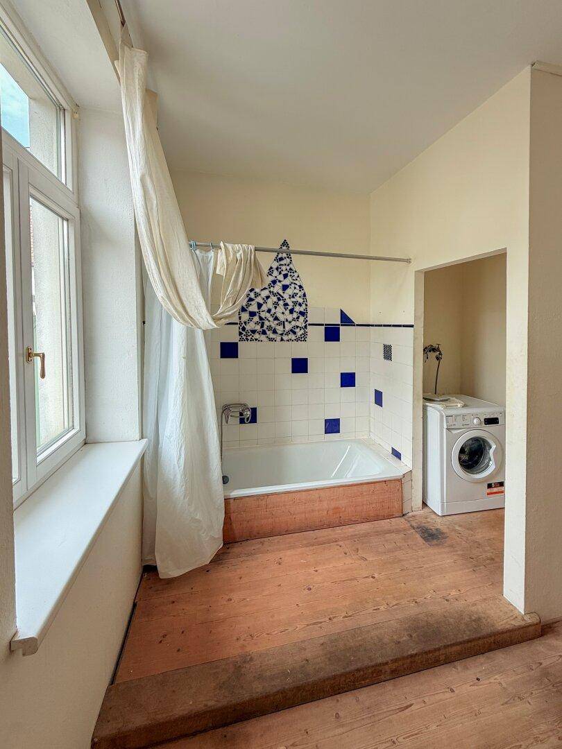Badezimmer mit Badewanne, Waschmaschine und einem Fenster, das viel Tageslicht spendet.