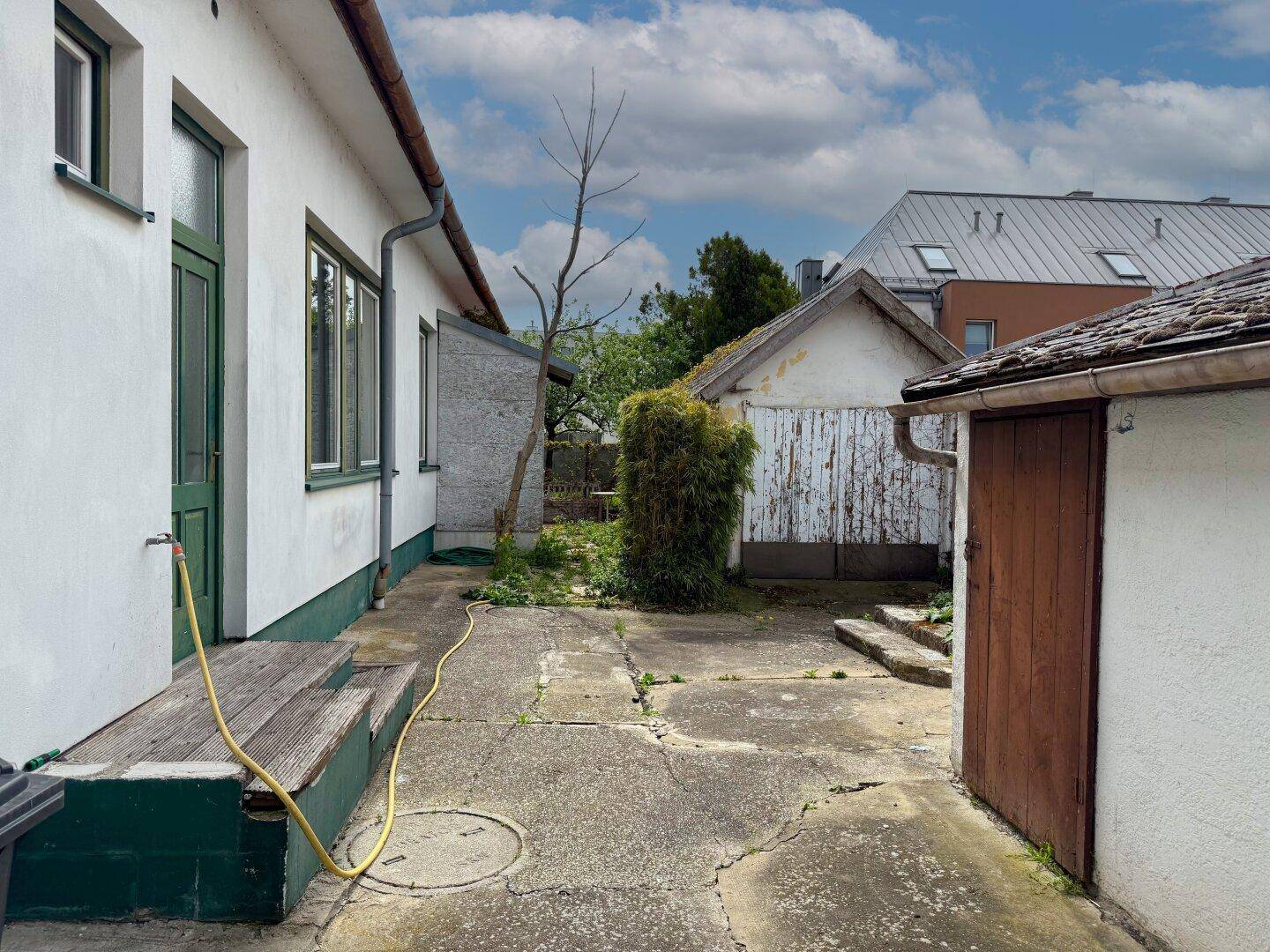 Gepflasterter Hinterhofbereich mit einem kleinen Schuppen und Zugang zum Garten.