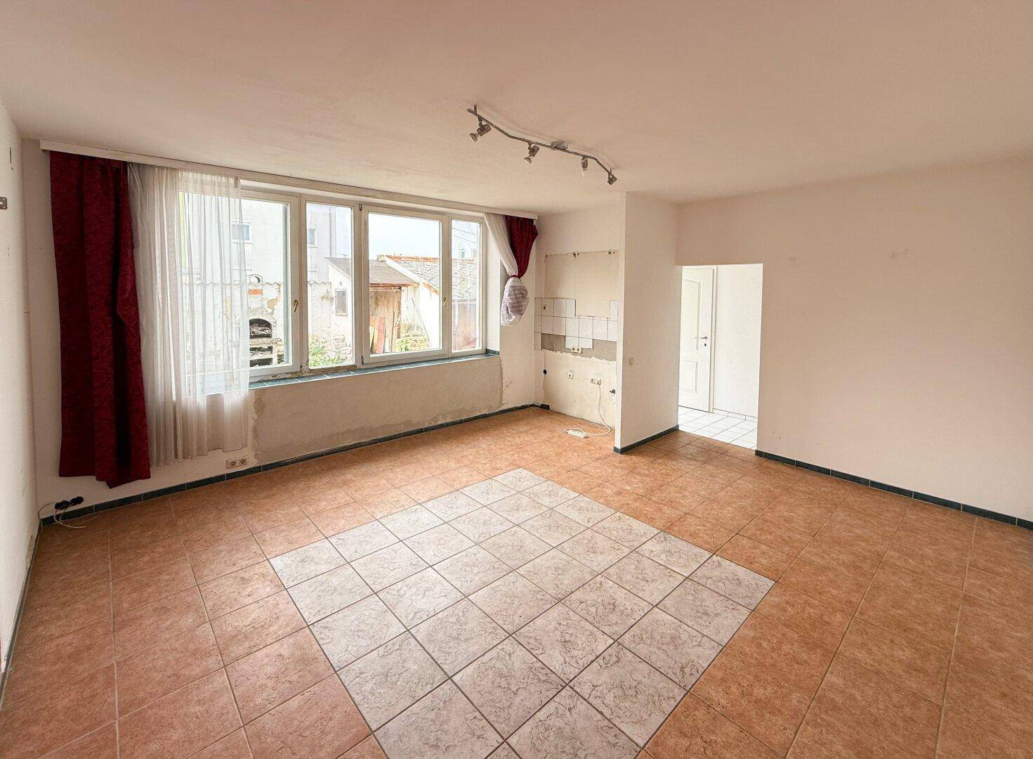 Geräumiger Raum mit Fliesenboden, großen Fenstern und einem Bereich für eine zukünftige Küchenzeile.