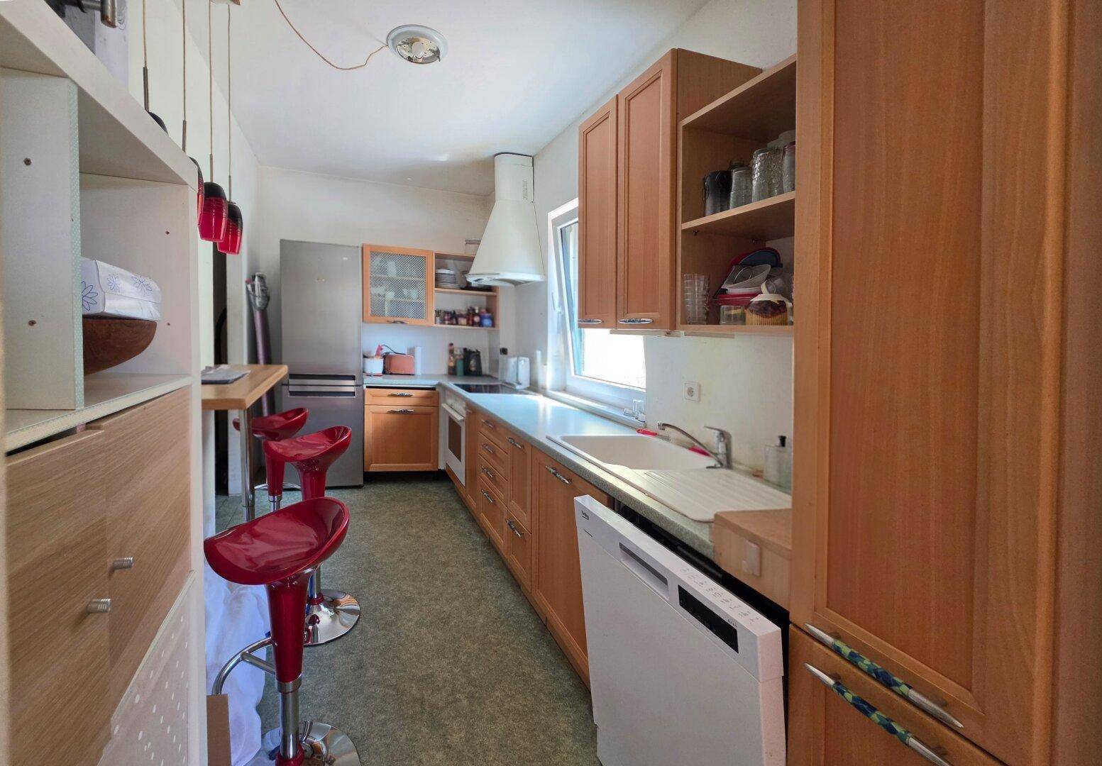 Längliche Küche mit Holzschränken, Frühstücksbar und modernen roten Barhockern.