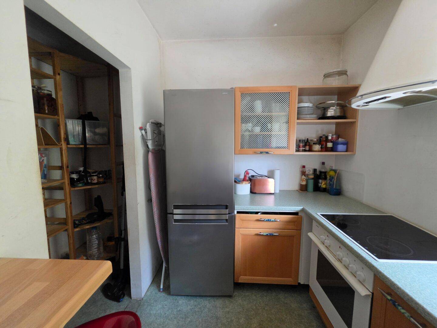 Küchenbereich mit Kühlschrank, Kochfeld und angrenzender Speisekammer mit Regalen.