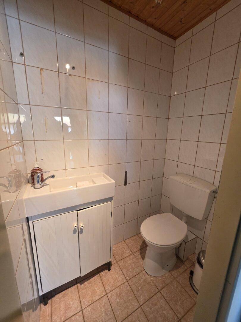 Kleines Gäste-WC mit weißen Fliesen, Holzdecke und einfacher Ausstattung.