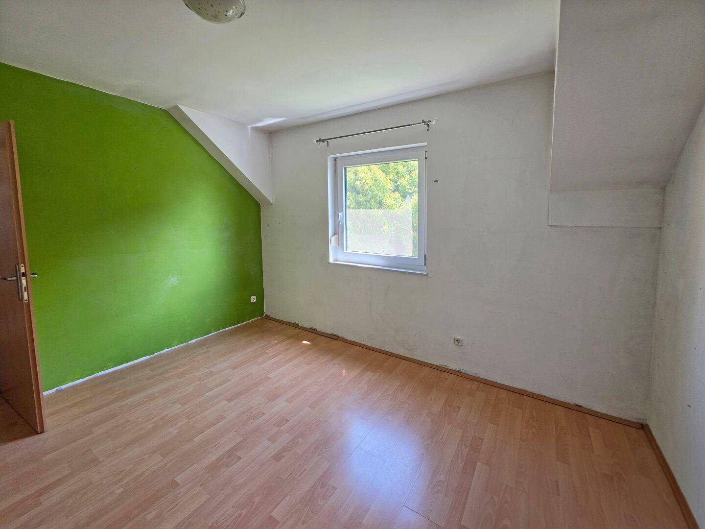 Leeres Schlafzimmer mit grüner Akzentwand, Laminatboden und Dachschräge.