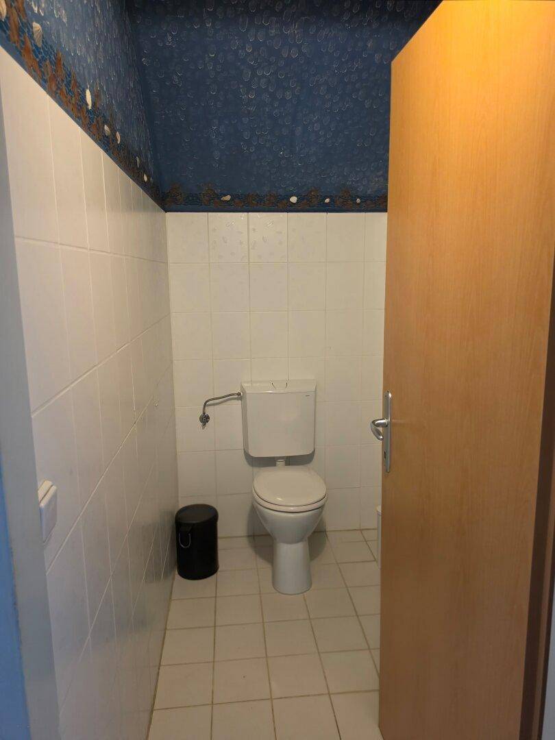 Einfaches WC mit weißen Fliesen und einer auffälligen blauen Tapete.