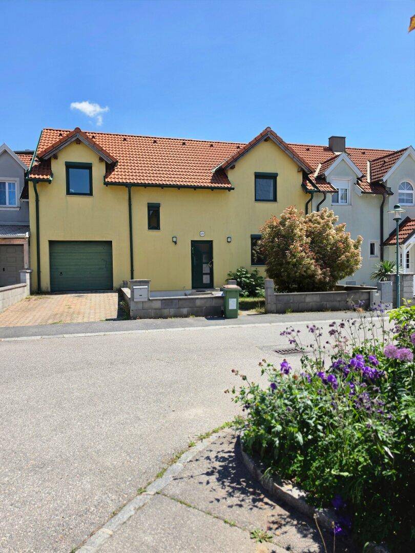 Gelbes Einfamilienhaus mit rotem Ziegeldach und Vorgarten an einer ruhigen Straße.
