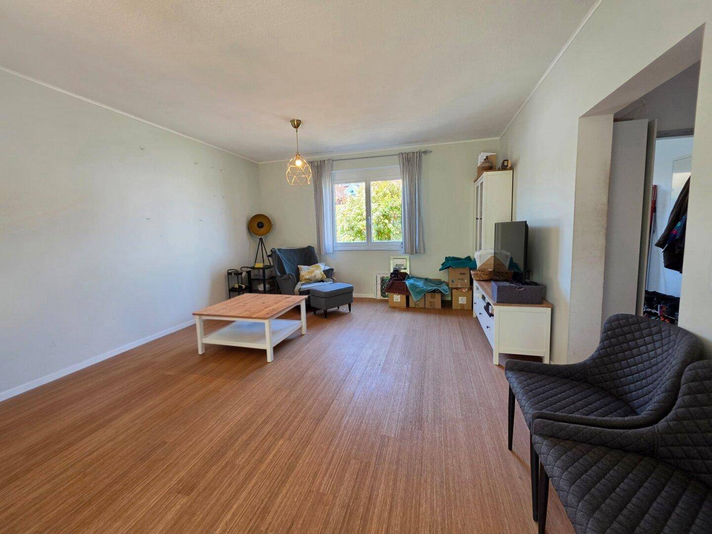 Geräumiges Wohnzimmer mit Laminatboden und Blick ins Grüne durch das Fenster.