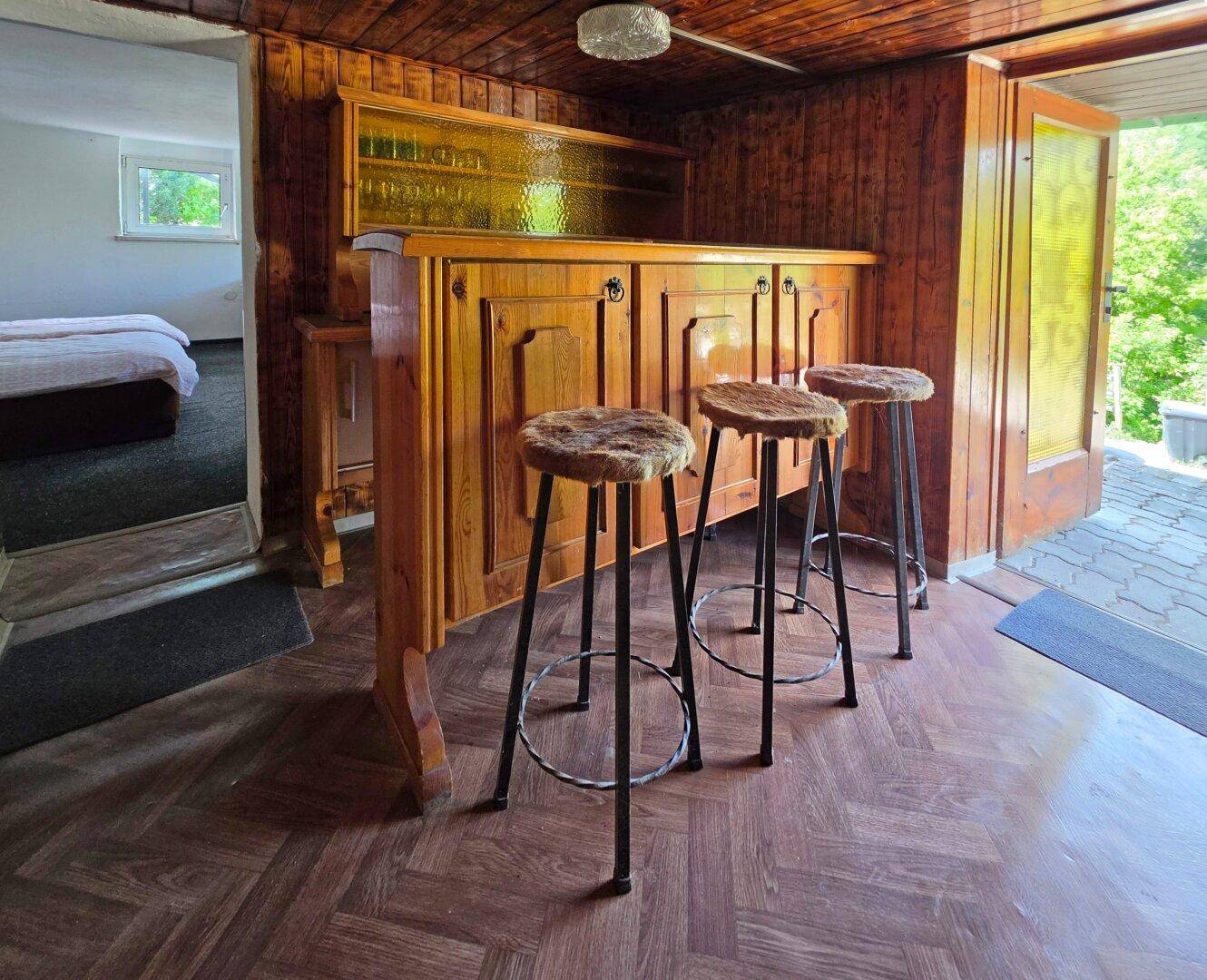 Rustikaler Barbereich mit Holzelementen, Barhockern und Zugang zur Terrasse.