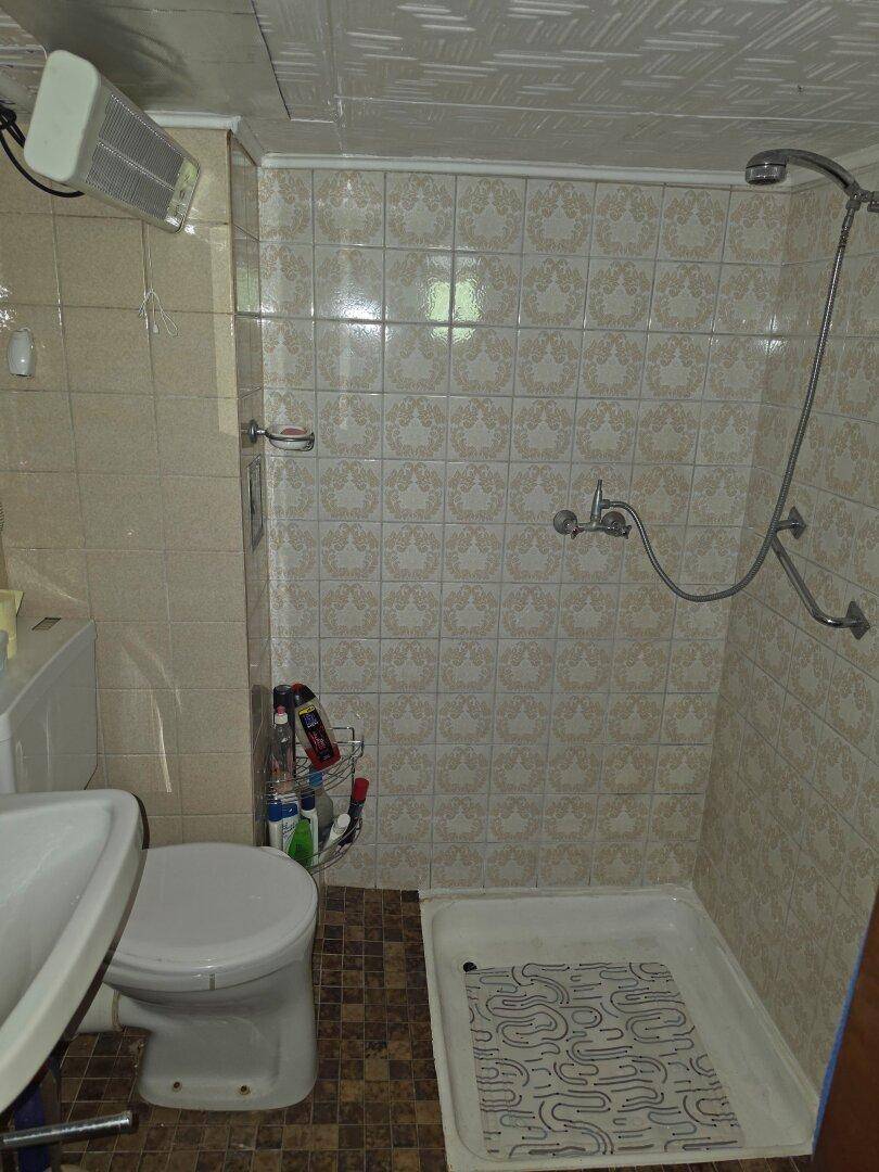 Funktionales Badezimmer mit Dusche, WC und hellen Fliesen im Retro-Stil.