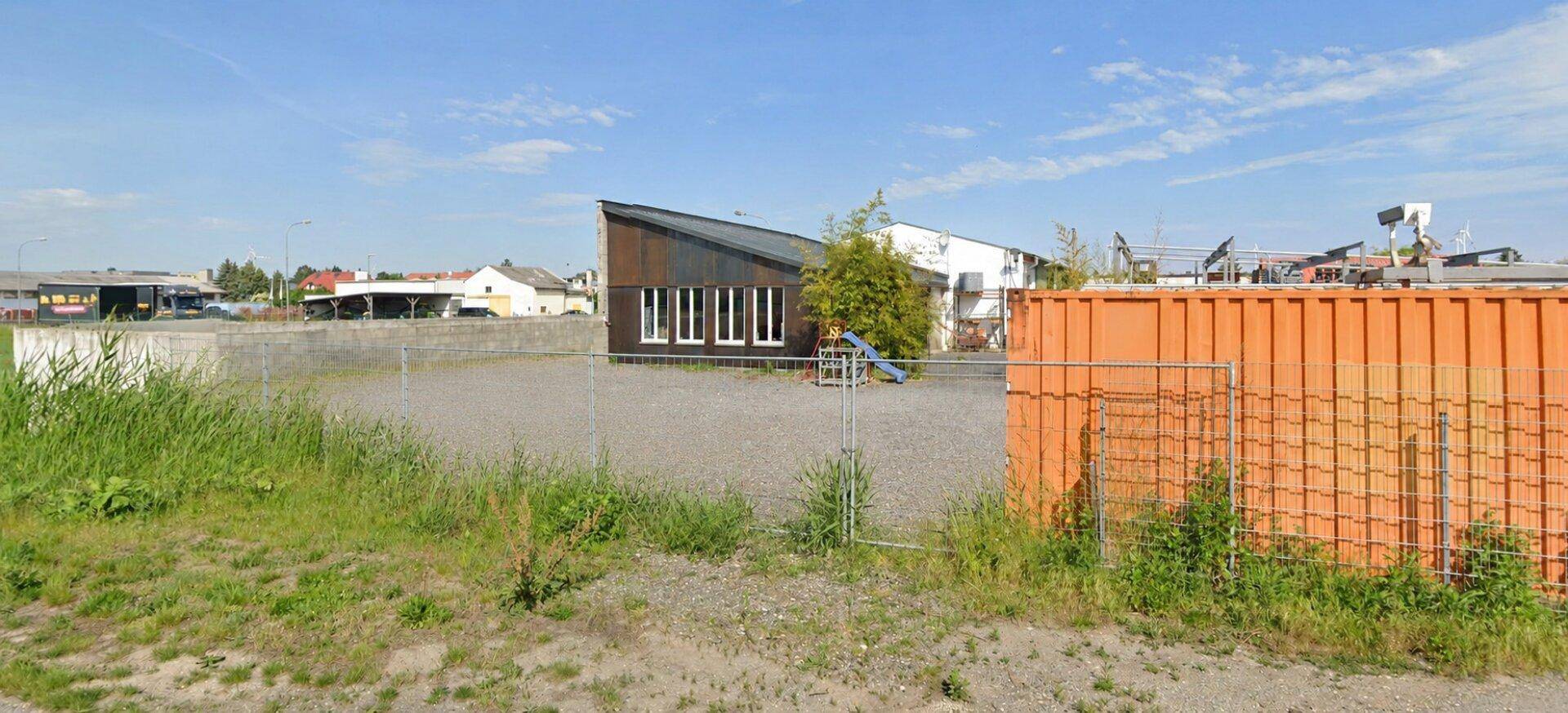 Außenansicht eines modernen Gebäudes mit schrägem Dach und weißen Fenstern auf einem Schotterplatz.