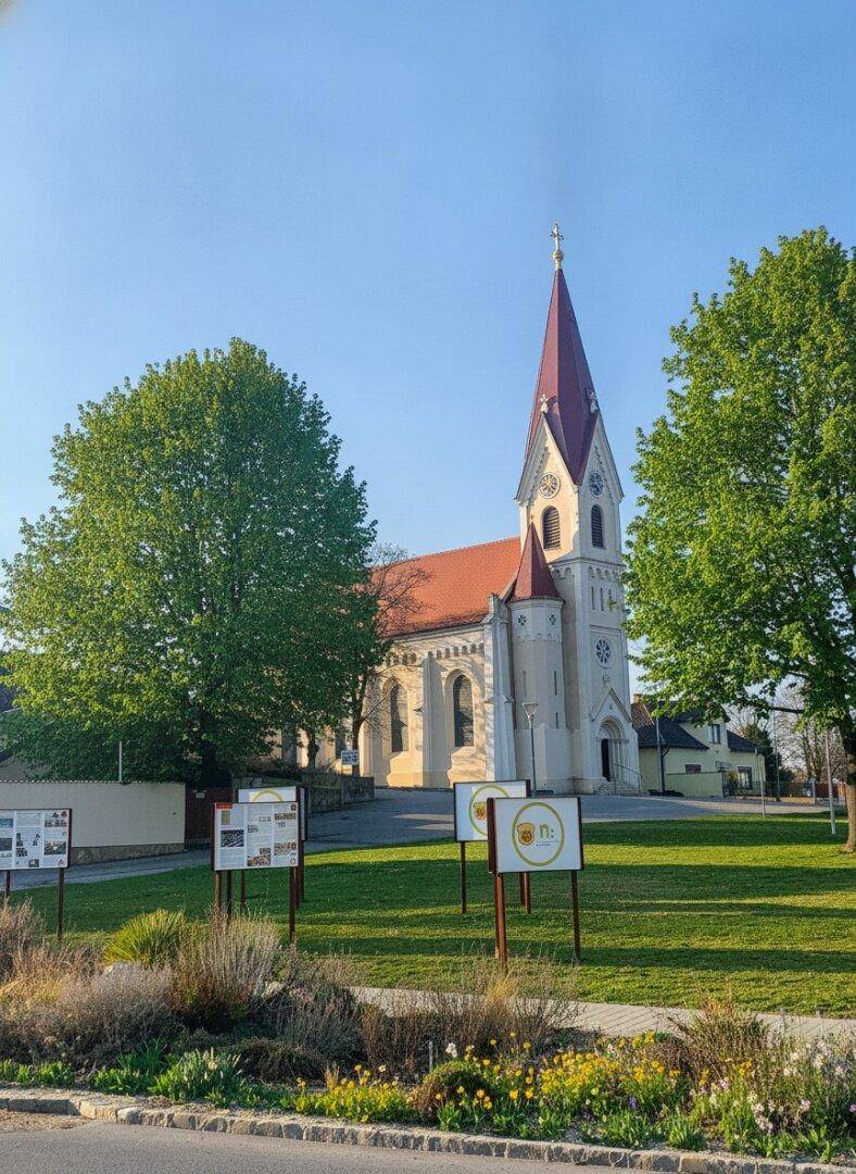 Historische Kirche mit rotem Turm und weißer Fassade, umgeben von Grünflächen.