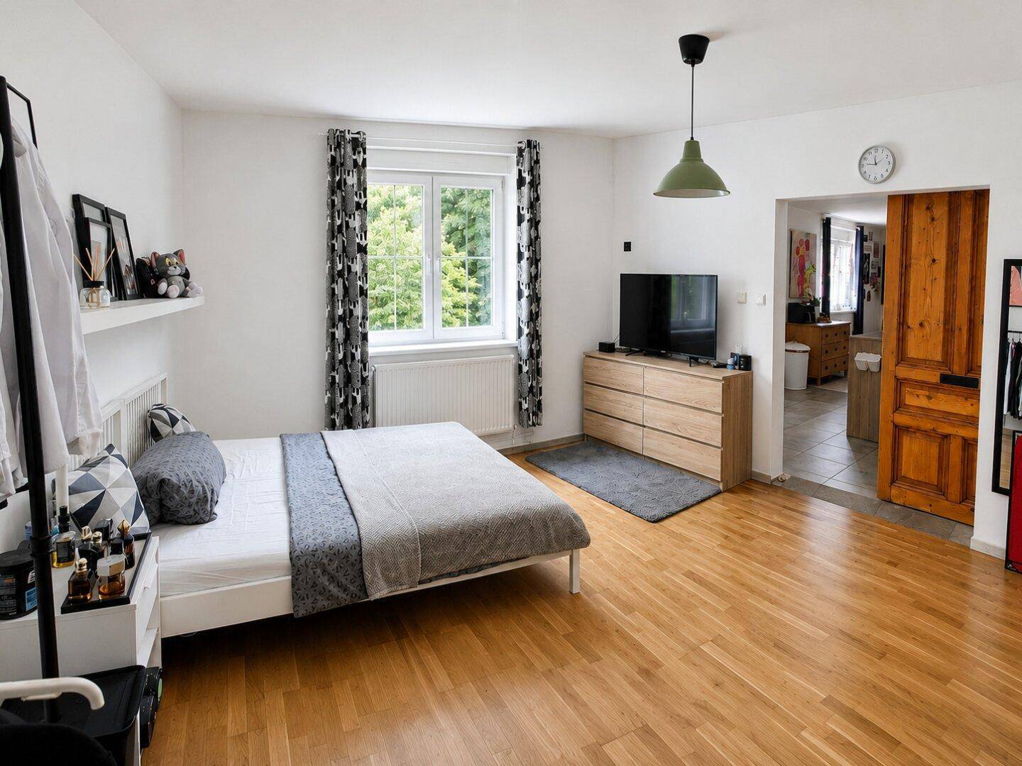 Geräumiges Schlafzimmer mit Holzboden, Doppelbett und Kommode unter einem Fenster mit Grünblick.