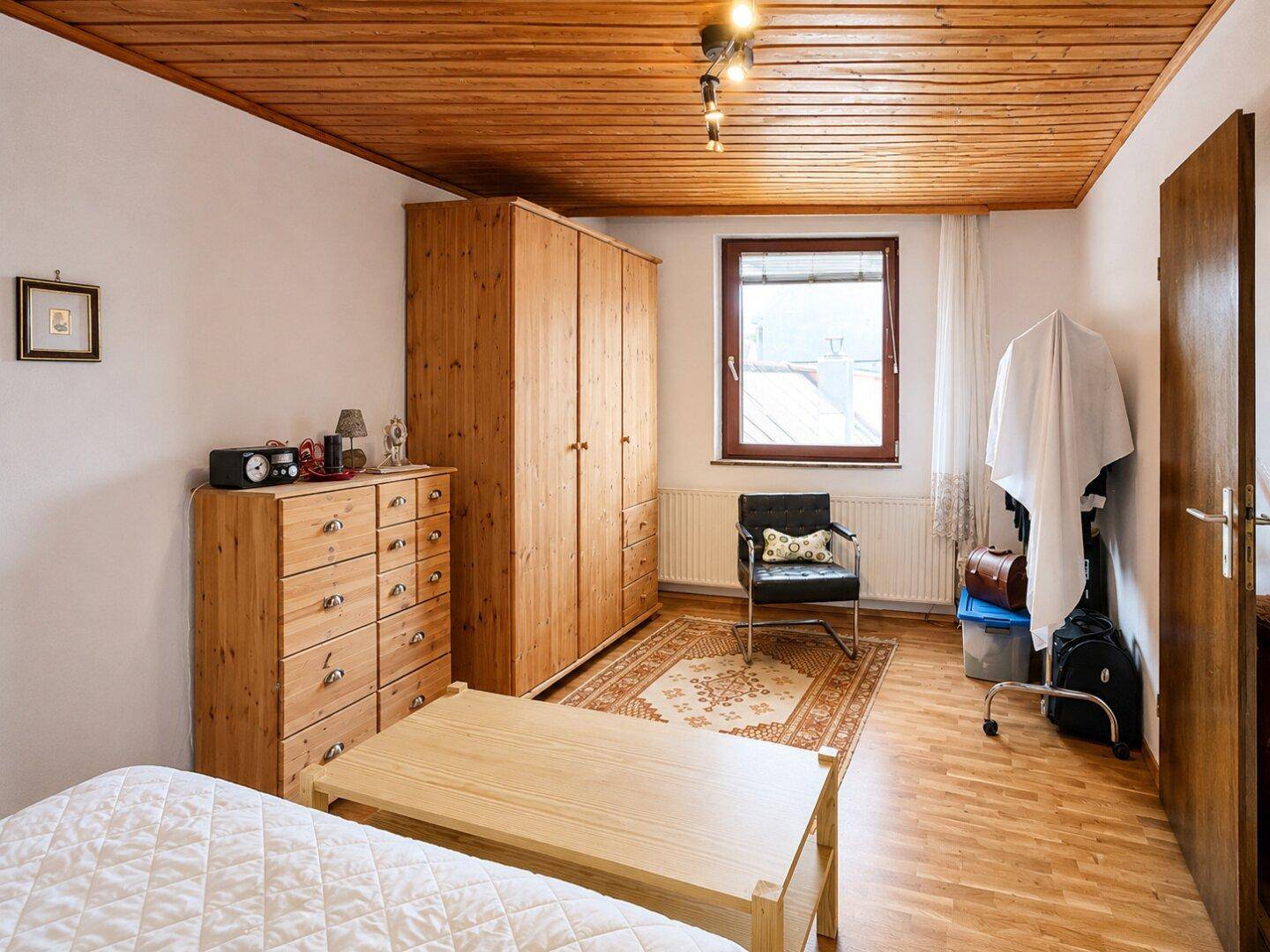 Gemütliches Schlafzimmer mit Holzboden, Holzdecke und Kleiderschrank, mit Blick nach draußen.