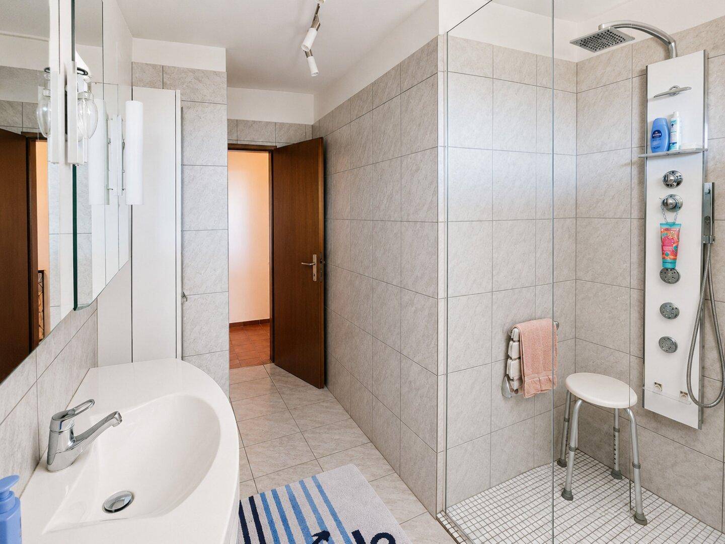 Modernes Badezimmer mit Duschkabine, Waschbecken und hellen Fliesen, gut beleuchtet.