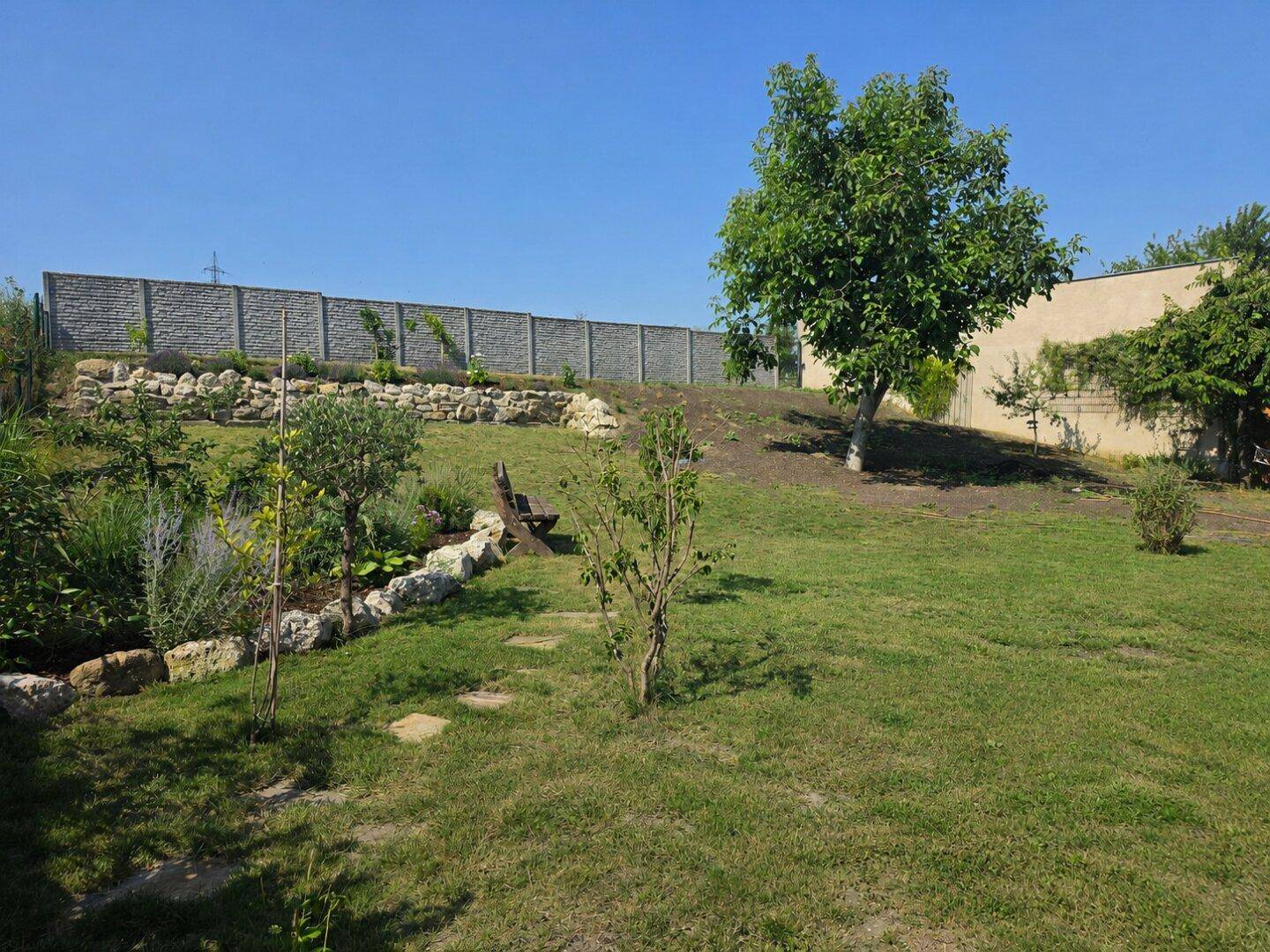 Großer, leicht abfallender Garten mit Rasenfläche, Steinmauern und einem Zaun im Hintergrund.