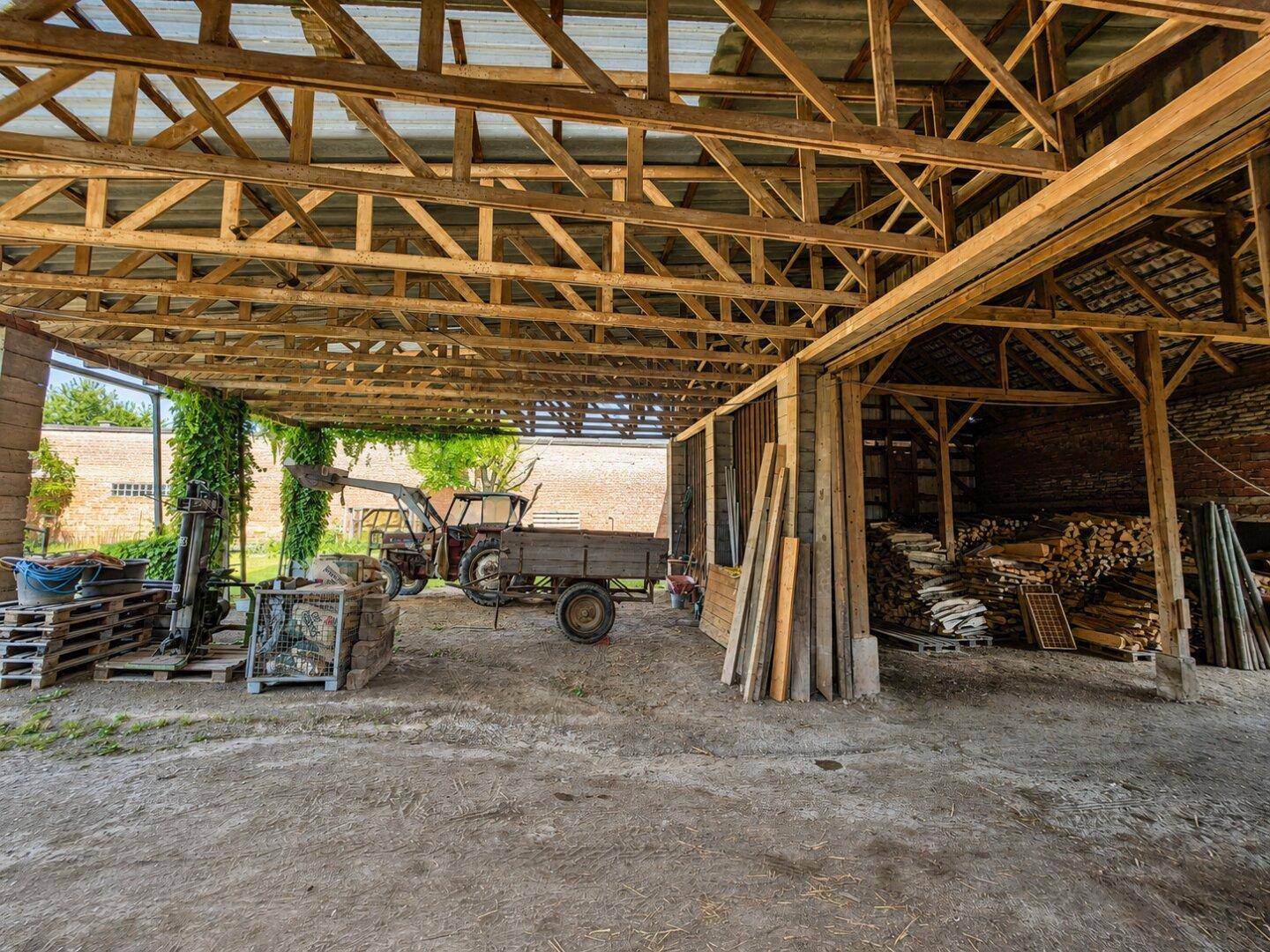 Offener Schuppenbereich mit Holzdachkonstruktion, Lagerung und landwirtschaftlichen Geräten.