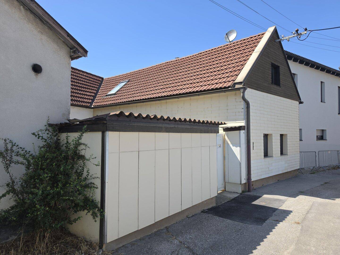 Außenansicht eines Gebäudes mit Ziegeldach und einem angebauten Schuppen.
