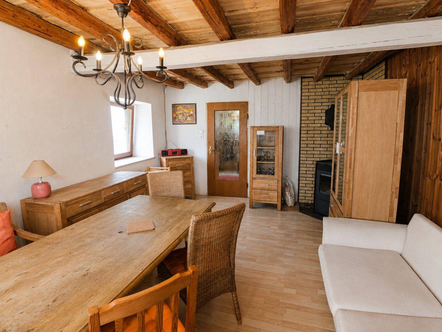 Rustikaler Wohn-Essbereich mit Holzbalken, Esstisch und bequemer Couch in ländlichem Stil.