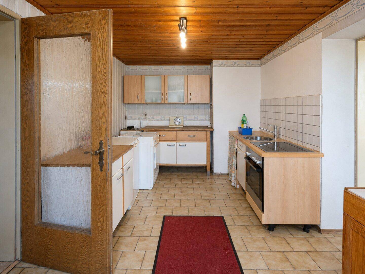 Funktionale Küche mit Fliesenboden, Holzdecke und älteren Einbauschränken.