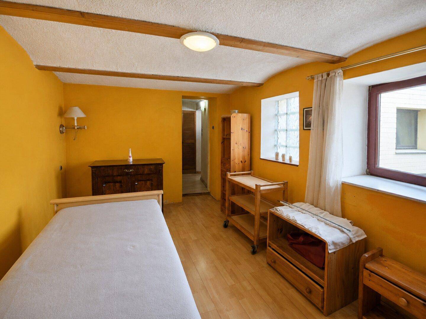 Helles Schlafzimmer mit gelben Wänden, Einzelbett und rustikalen Holzmöbeln.