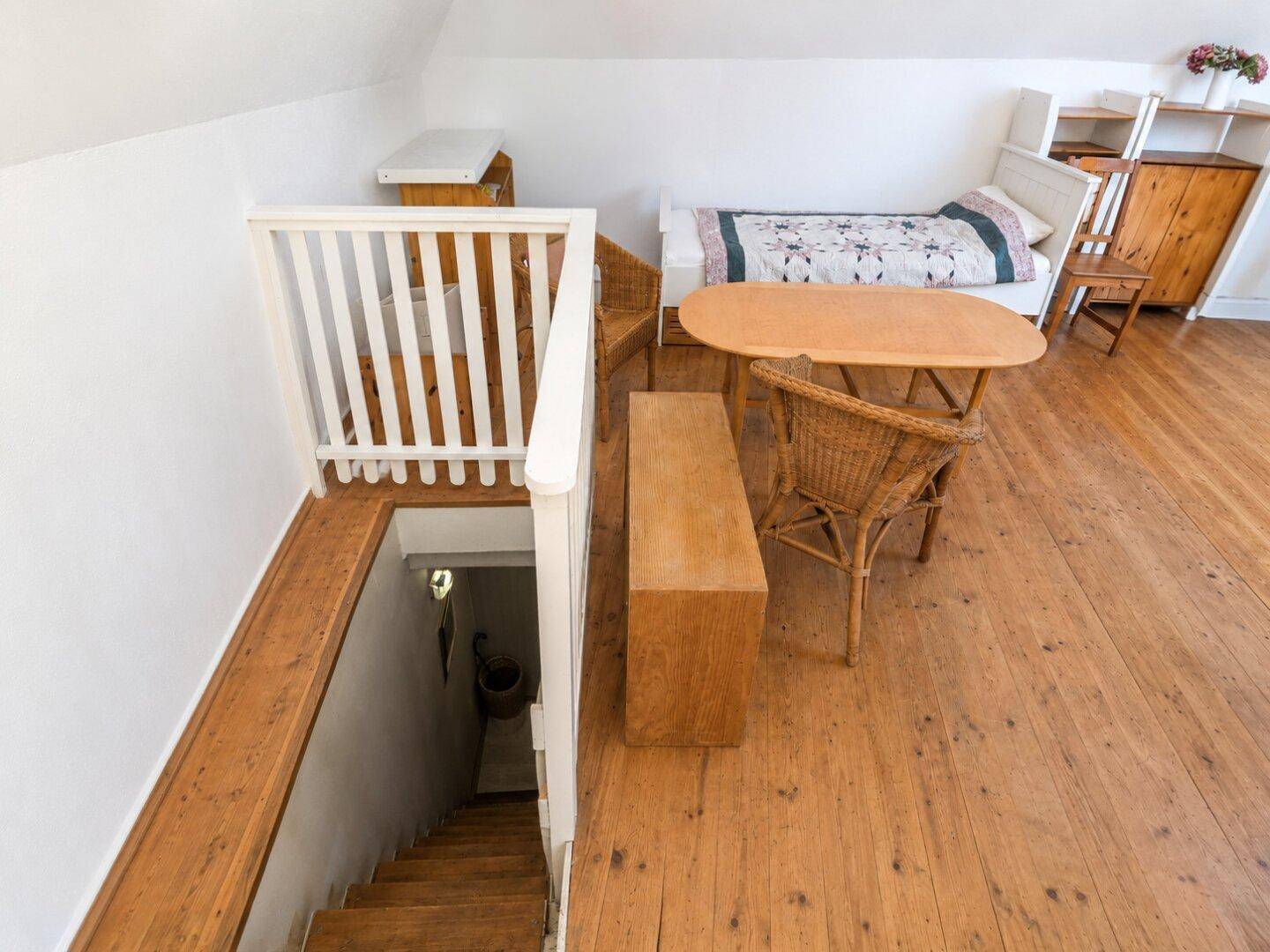 Gemütlicher Dachbodenbereich mit Holzboden, Schlafgelegenheit und Treppenzugang.
