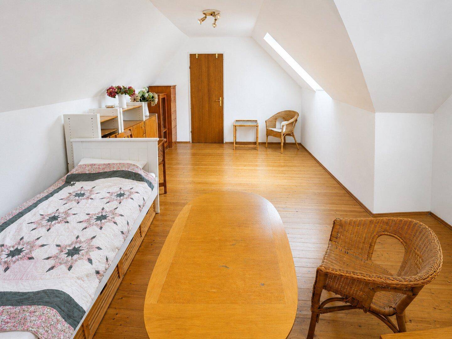 Heller Dachbodenraum mit Holzboden, Einzelbett und Dachfenster für natürliches Licht.