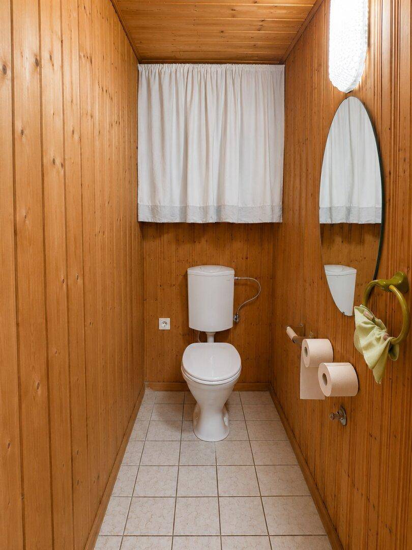 Kleines WC mit Holzvertäfelung, Fliesenboden und schlichtem Design.