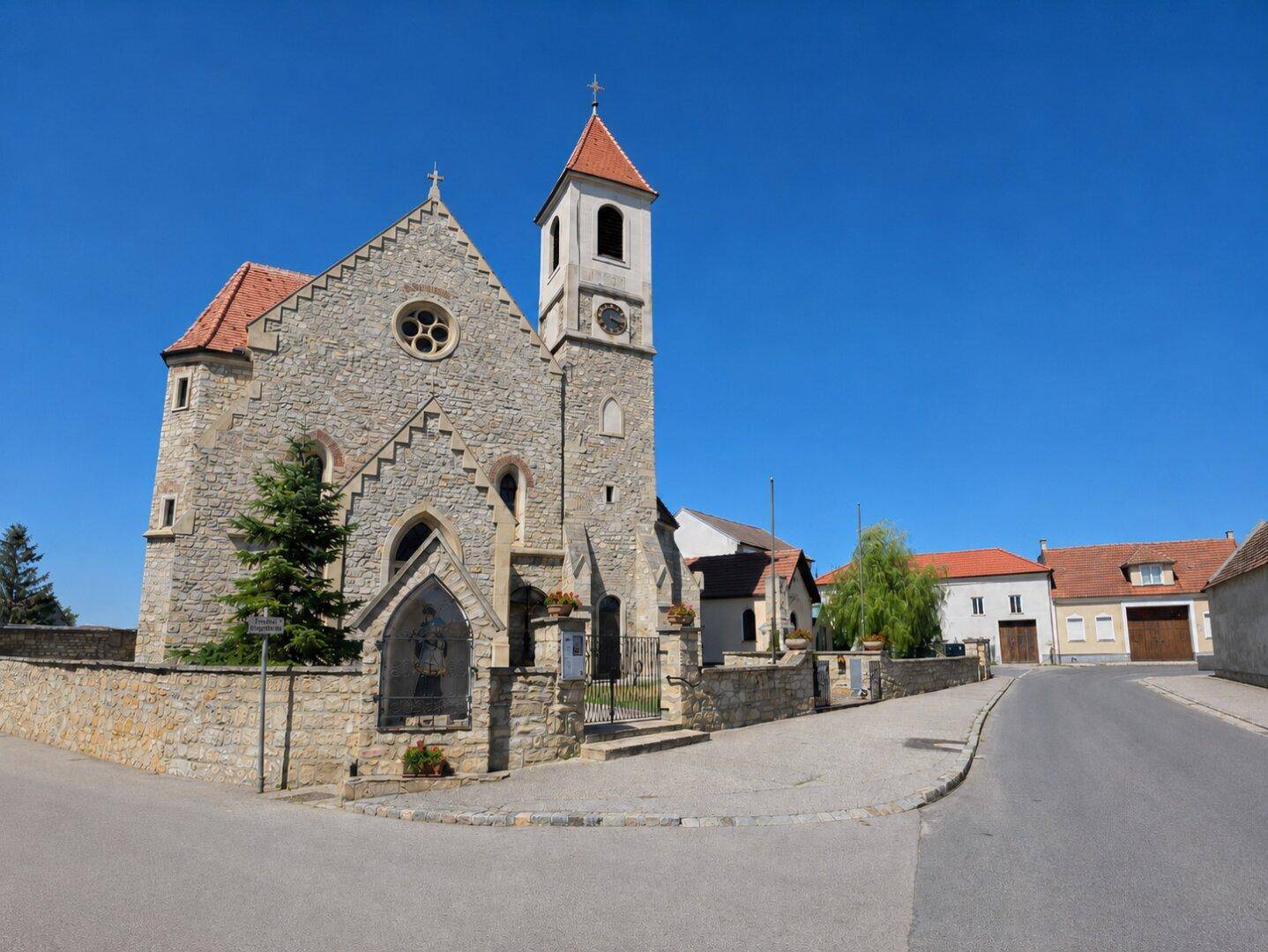 Historische Kirche mit Steinfassade und Glockenturm in einer ländlichen Umgebung.