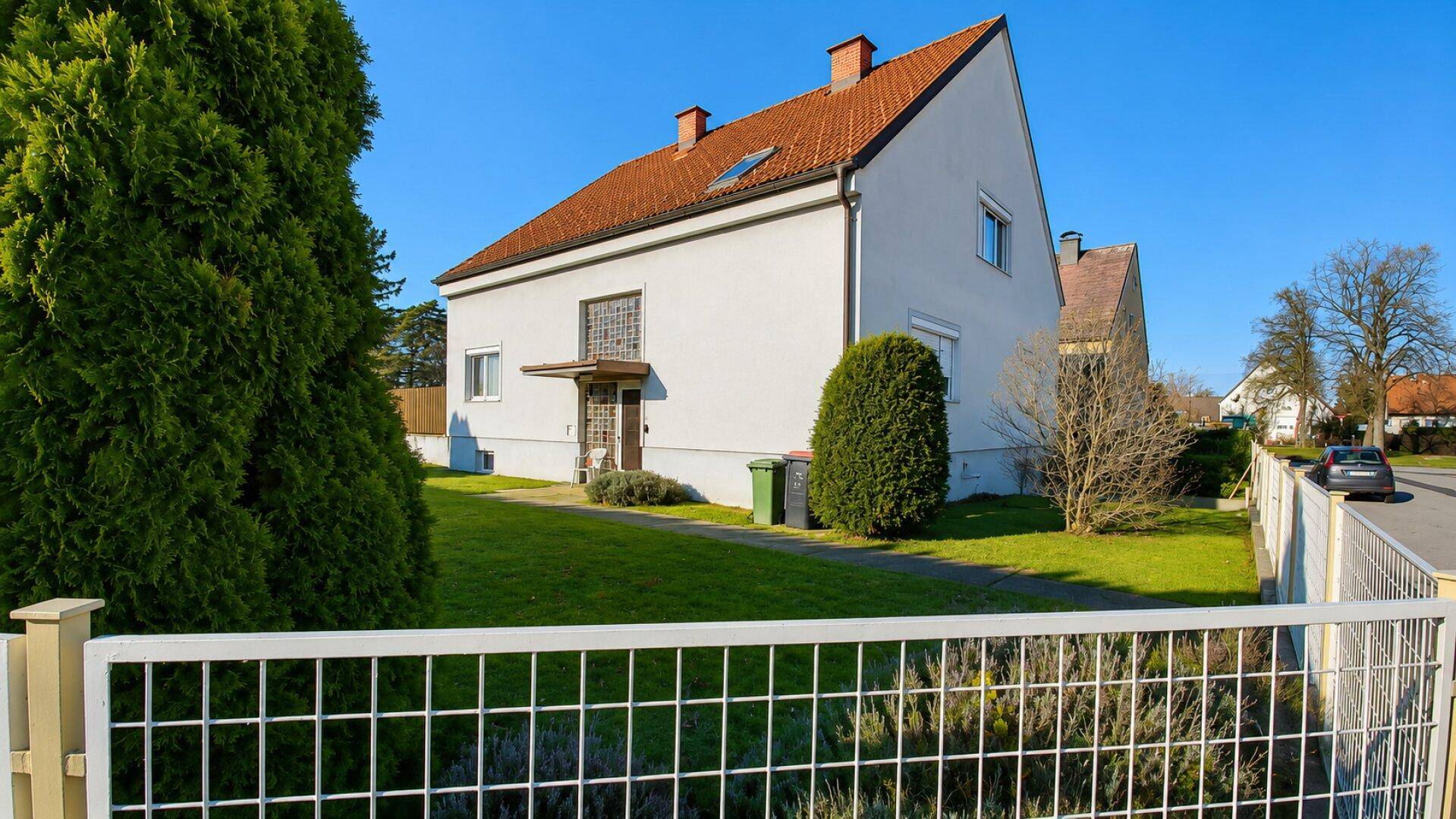 Ansicht des Einfamilienhauses von der Straßenseite mit Vorgarten und Zaun.