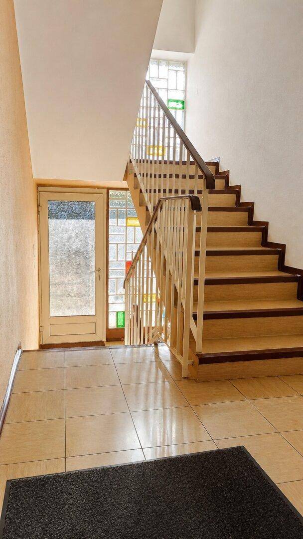 Heller Treppenaufgang mit Holzstufen, Geländer und farbigen Glasfenstern.