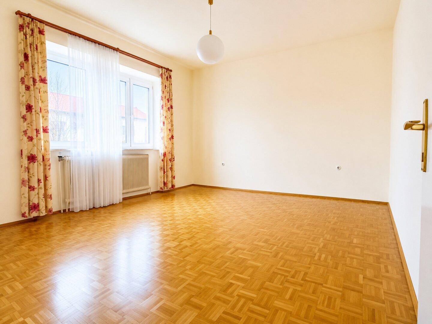 Helles, leeres Zimmer mit Parkettboden und großen Fenstern, bereit zur Einrichtung.