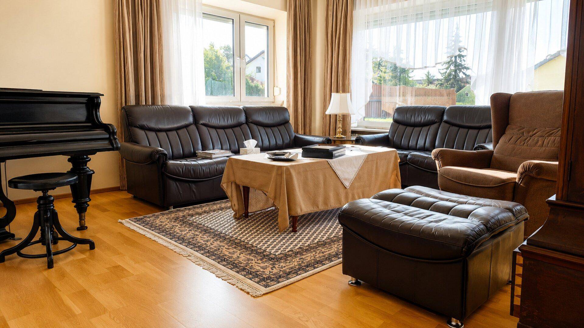 Gemütliches Wohnzimmer mit dunklen Ledersofas, Holzboden und einem Klavier.