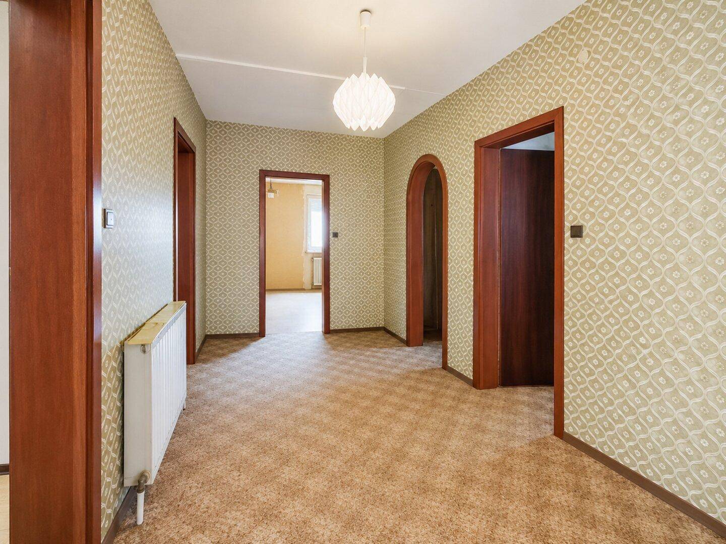 Geräumiger Flur mit gemusterter Tapete, Teppichboden und Holztüren.
