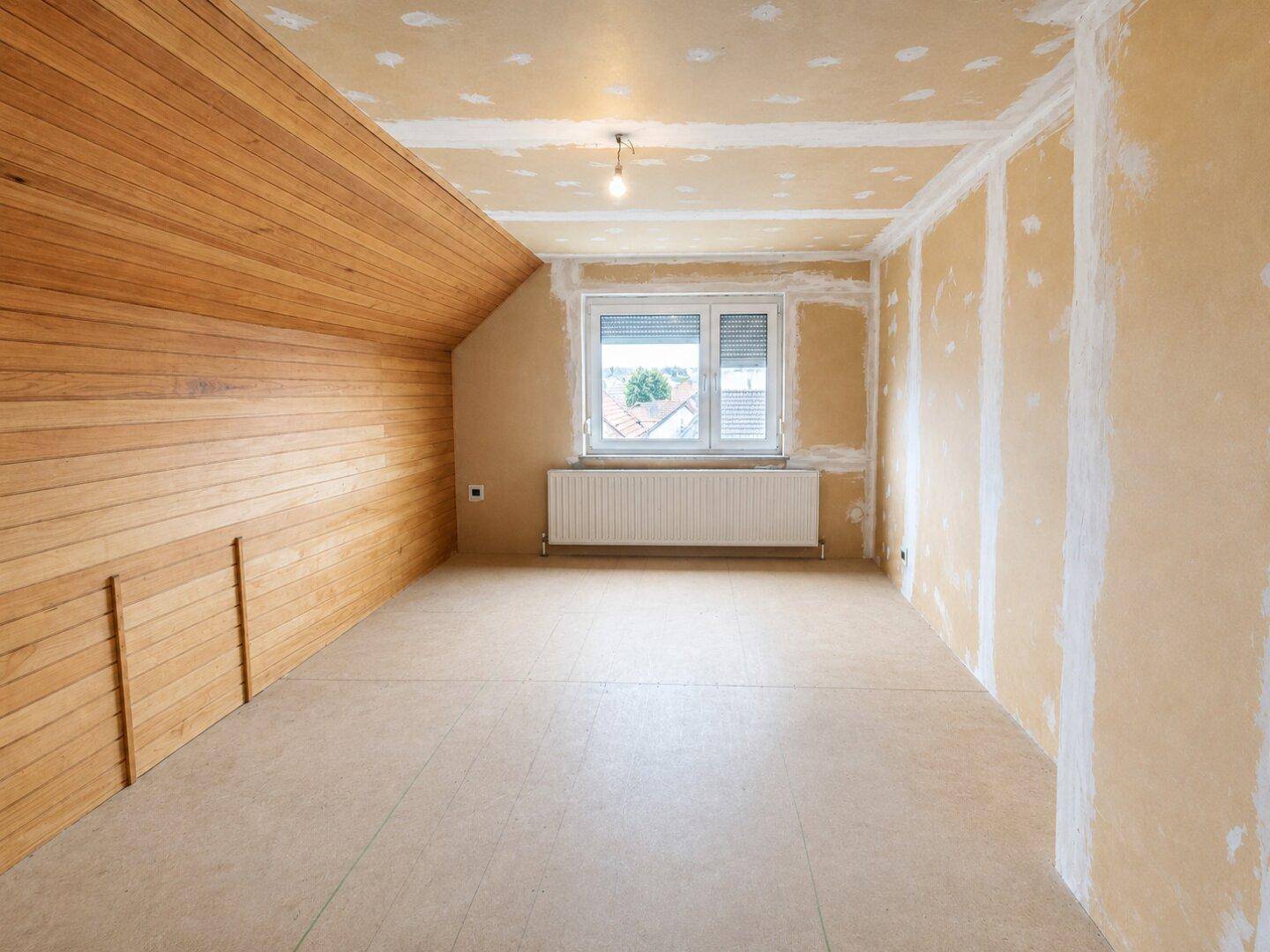 Dachzimmer im Rohbau mit Holzverkleidung und Fenster, bereit für den Ausbau.