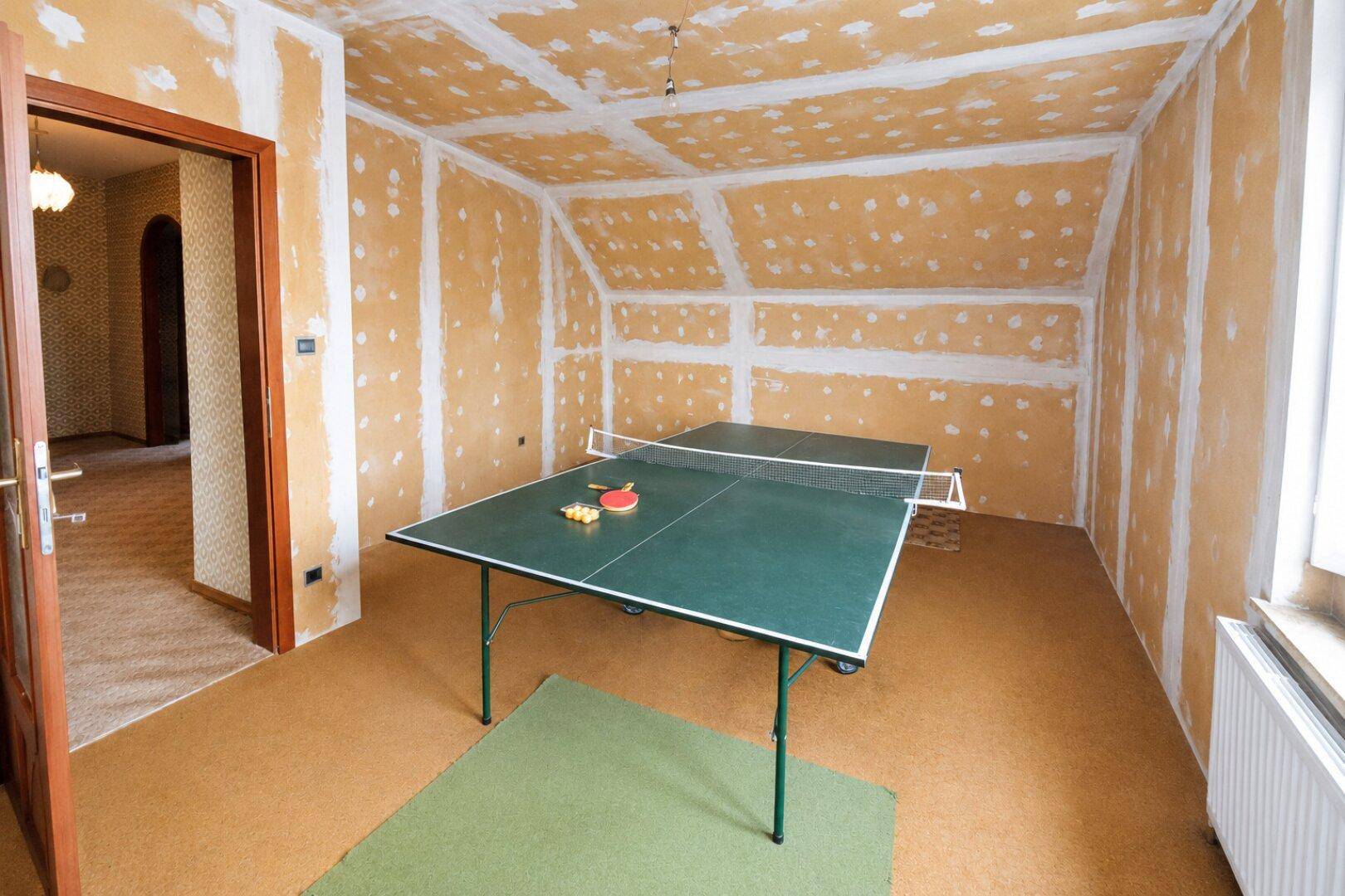 Dachzimmer mit Tischtennisplatte und Teppichboden, ideal als Spiel- oder Hobbyraum.