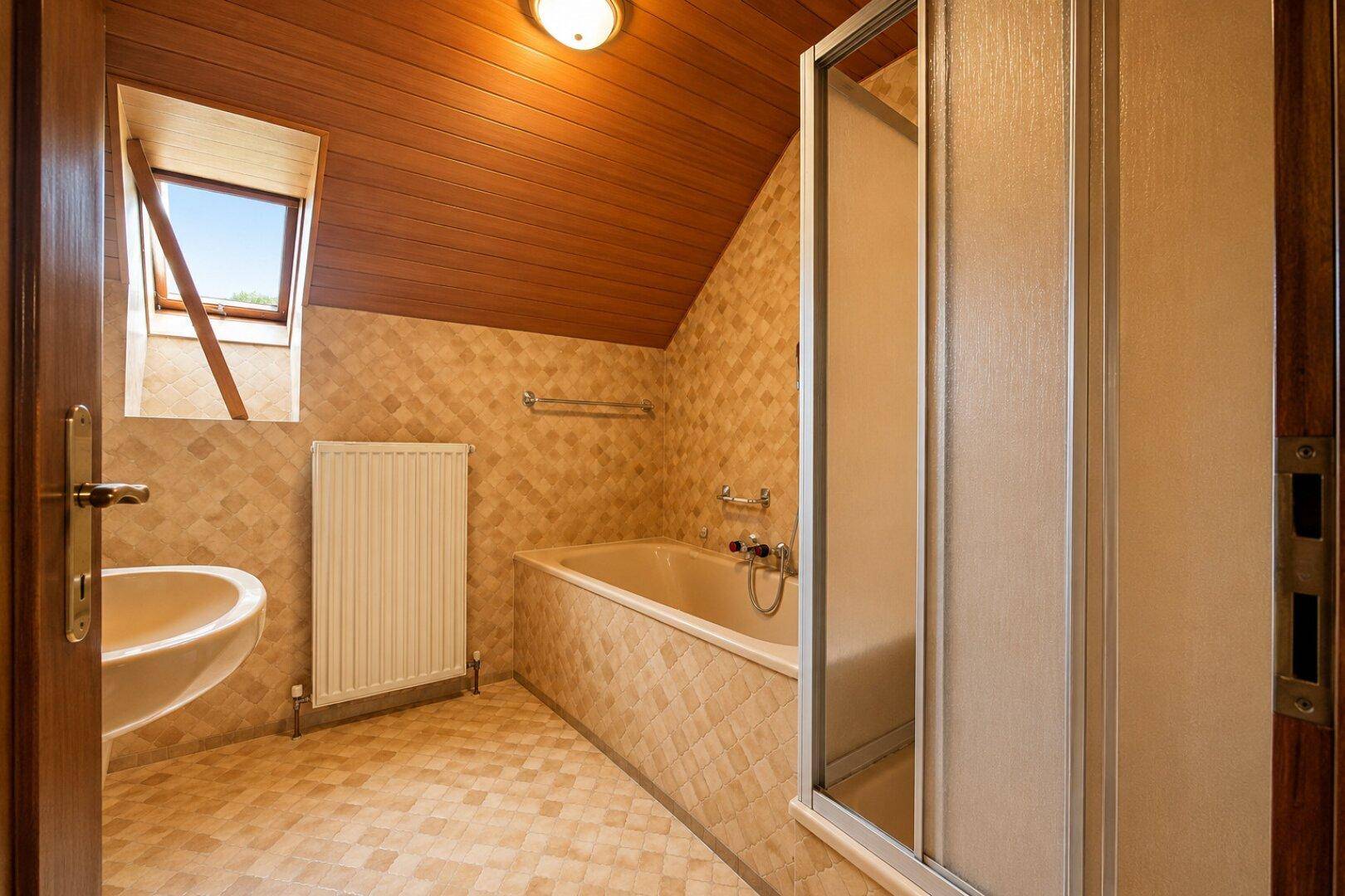 Badezimmer im Dachgeschoss mit Badewanne, Dusche und Dachfenster.