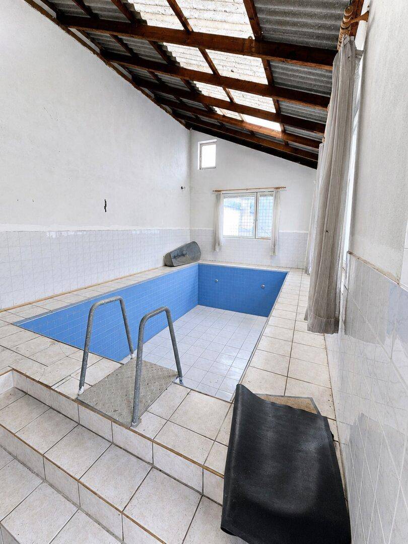 Innenpoolbereich mit gefliestem Becken, Holzdecke und sichtbaren Dachbalken.