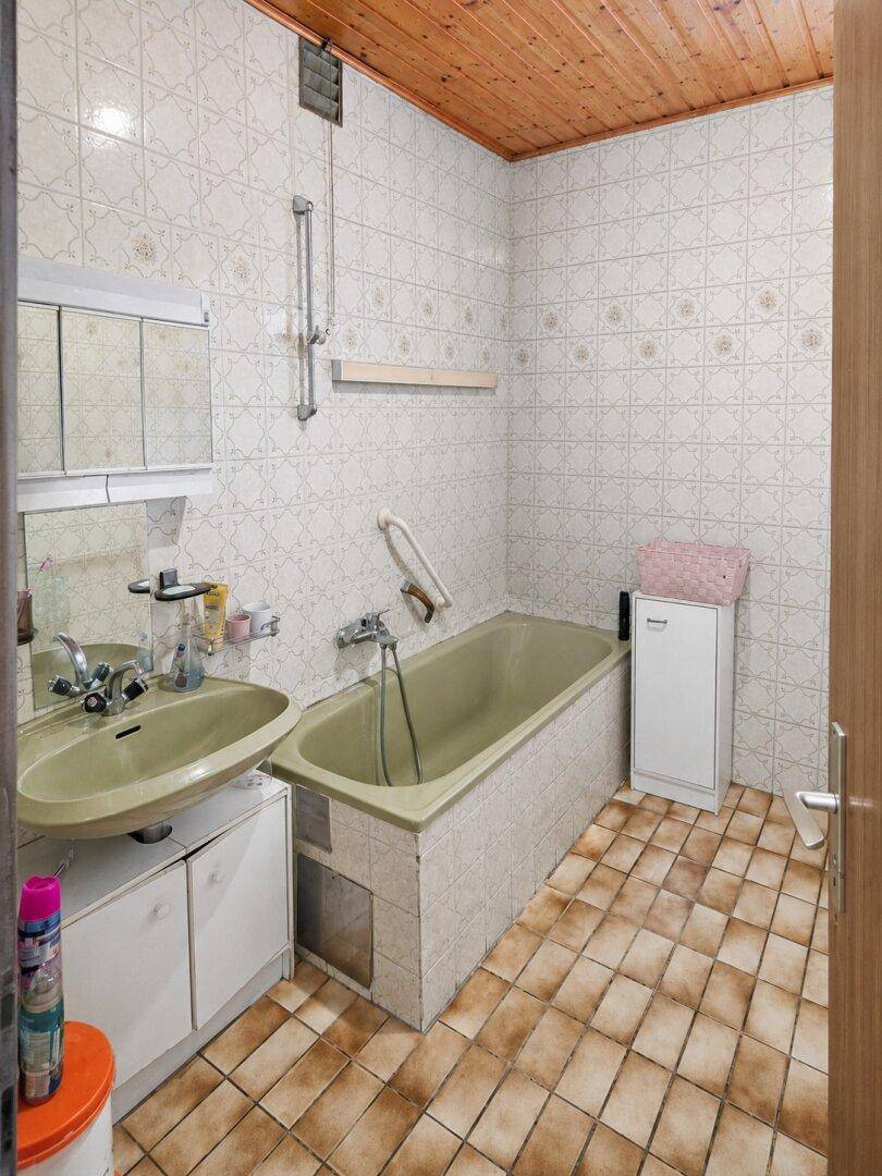 Badezimmer mit Badewanne, Waschbecken, Haltegriffen und Holzdecke.